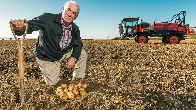 Robert kendal kneeling on farm next potatoes with a sprayer in the background